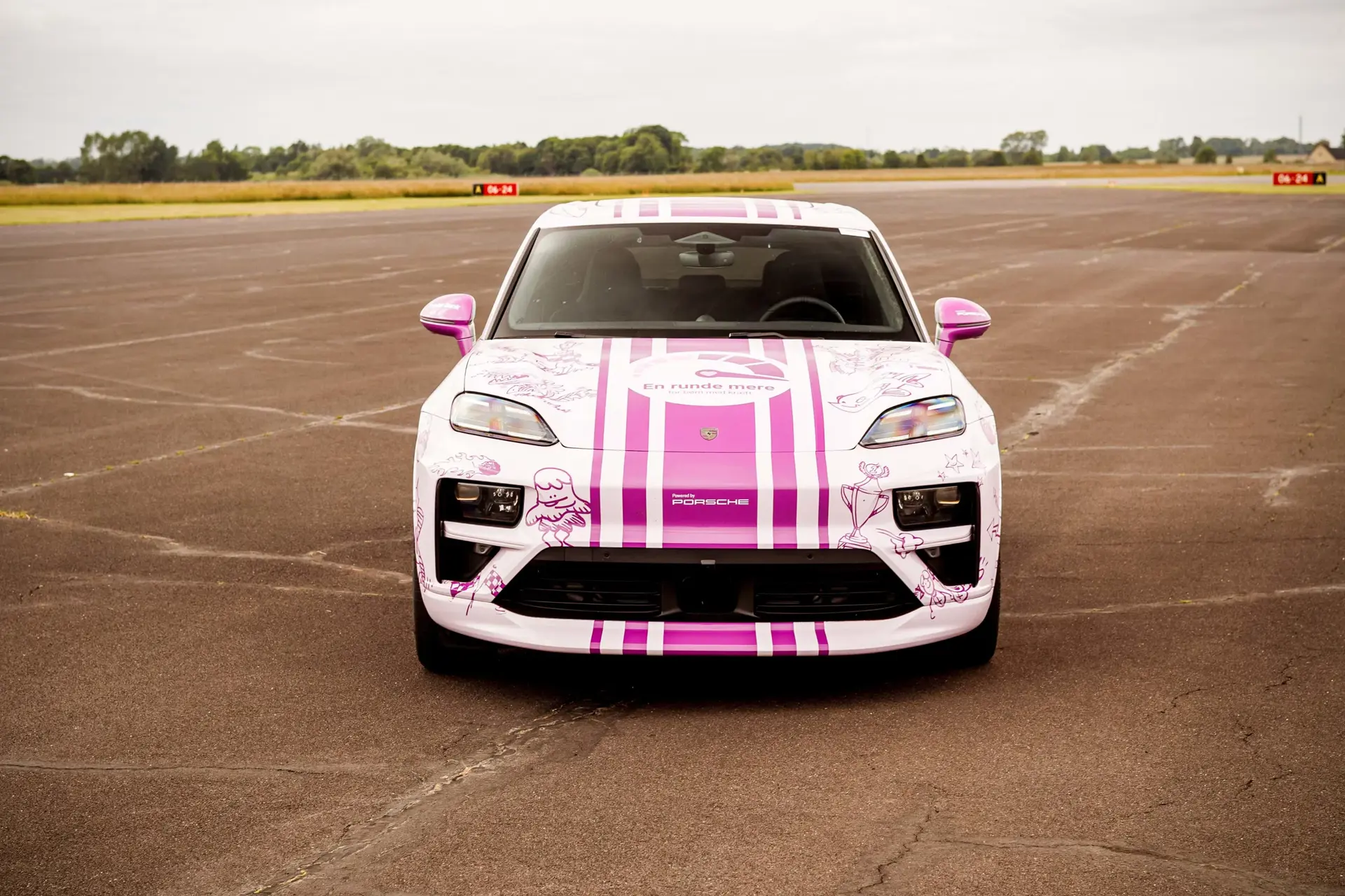 Hvid og pink sportsvogn med striber og illustrationer står midt på en tom racerbane.