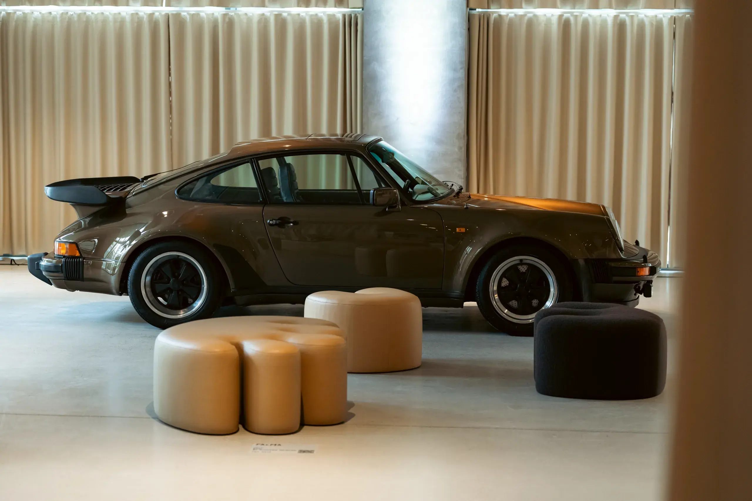 Bagenden af en hvid Porsche sportsvogn ses indendørs med bløde gardiner og loftpaneler i baggrunden.