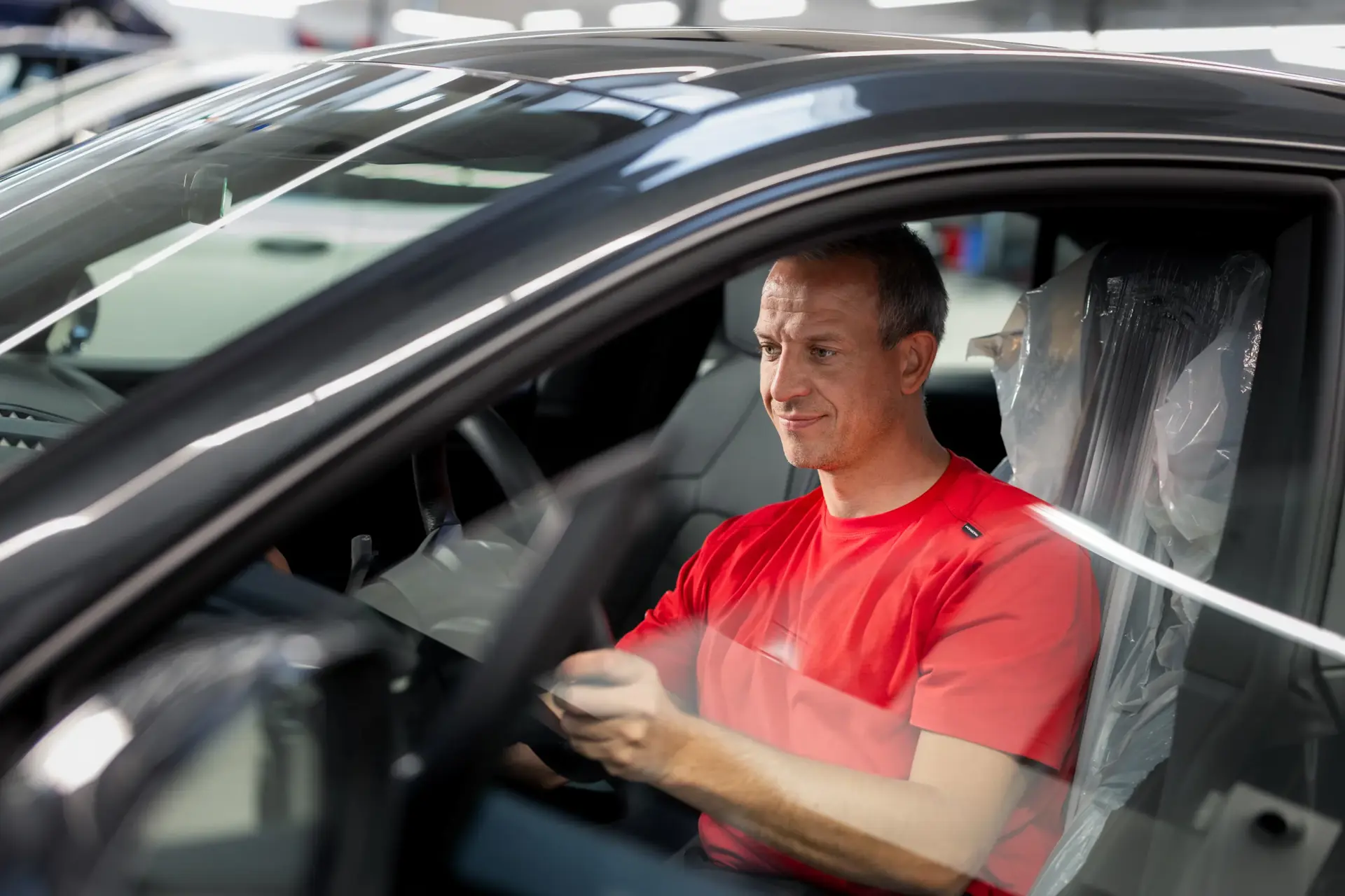 Mekaniker i rød trøje sidder i en bil i et Porsche-værksted og tester bilens funktioner.