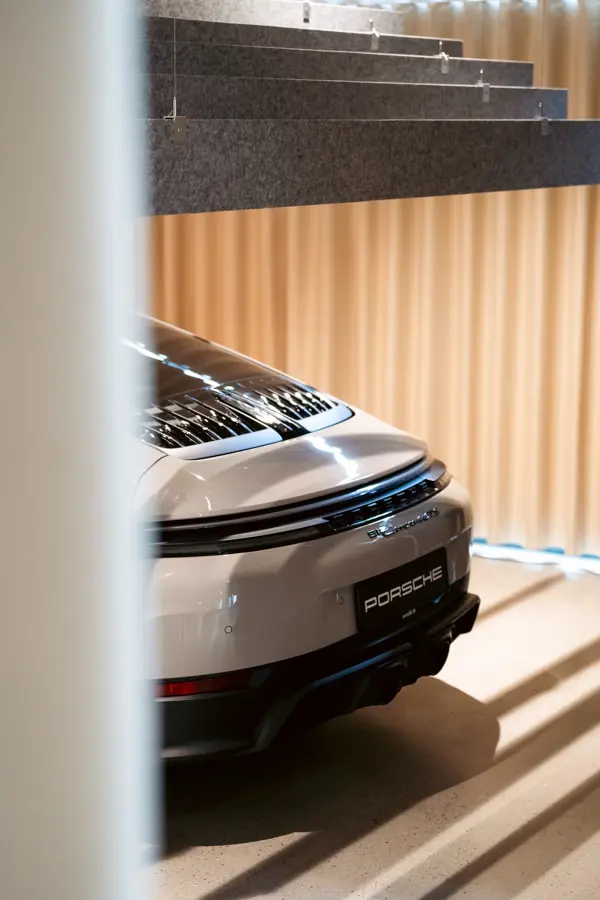 Bagenden af en hvid Porsche sportsvogn ses indendørs med bløde gardiner og loftpaneler i baggrunden.