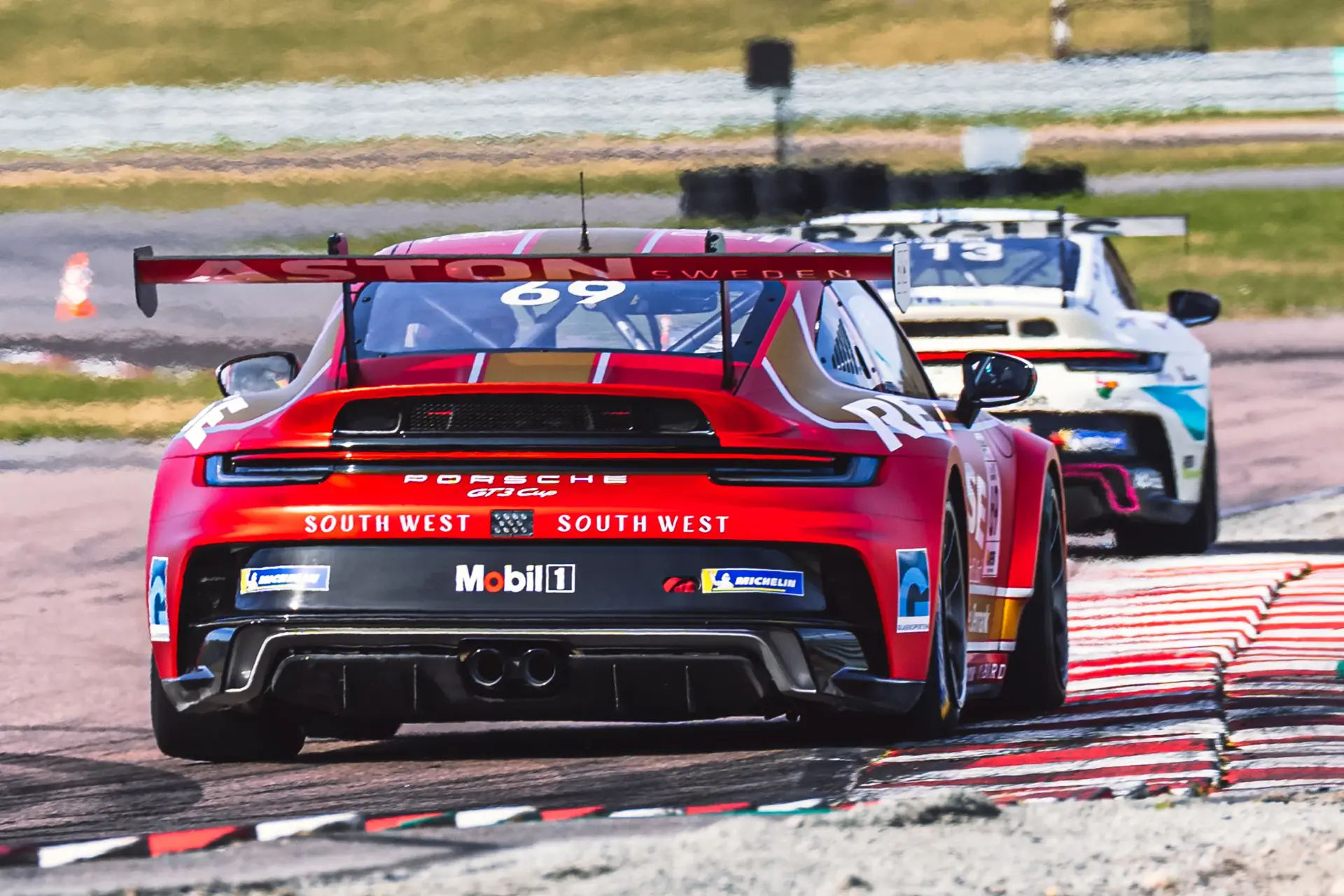 To racerbiler i en Porsche GT3 Cup-race kører tæt på hinanden rundt i et sving på banen.