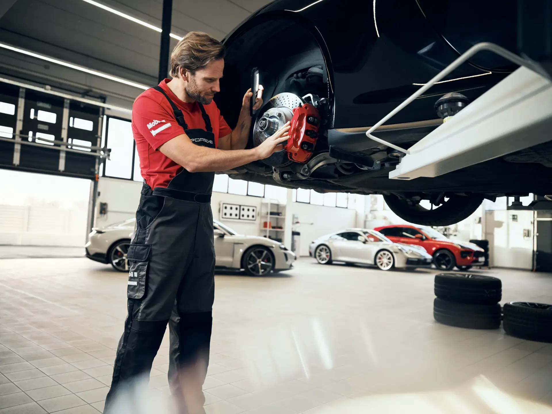 Mekaniker inspicerer bremsesystemet på en ophøjet Porsche i et lyst autoværksted.
