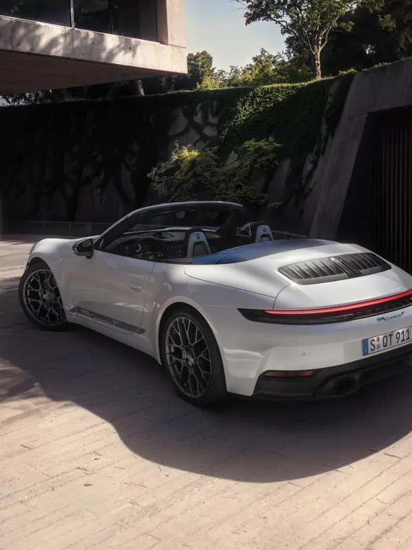 En hvid Porsche 911 Carrera T cabriolet holder parkeret udendørs foran en moderne bygning med grøn bevoksning på murene.