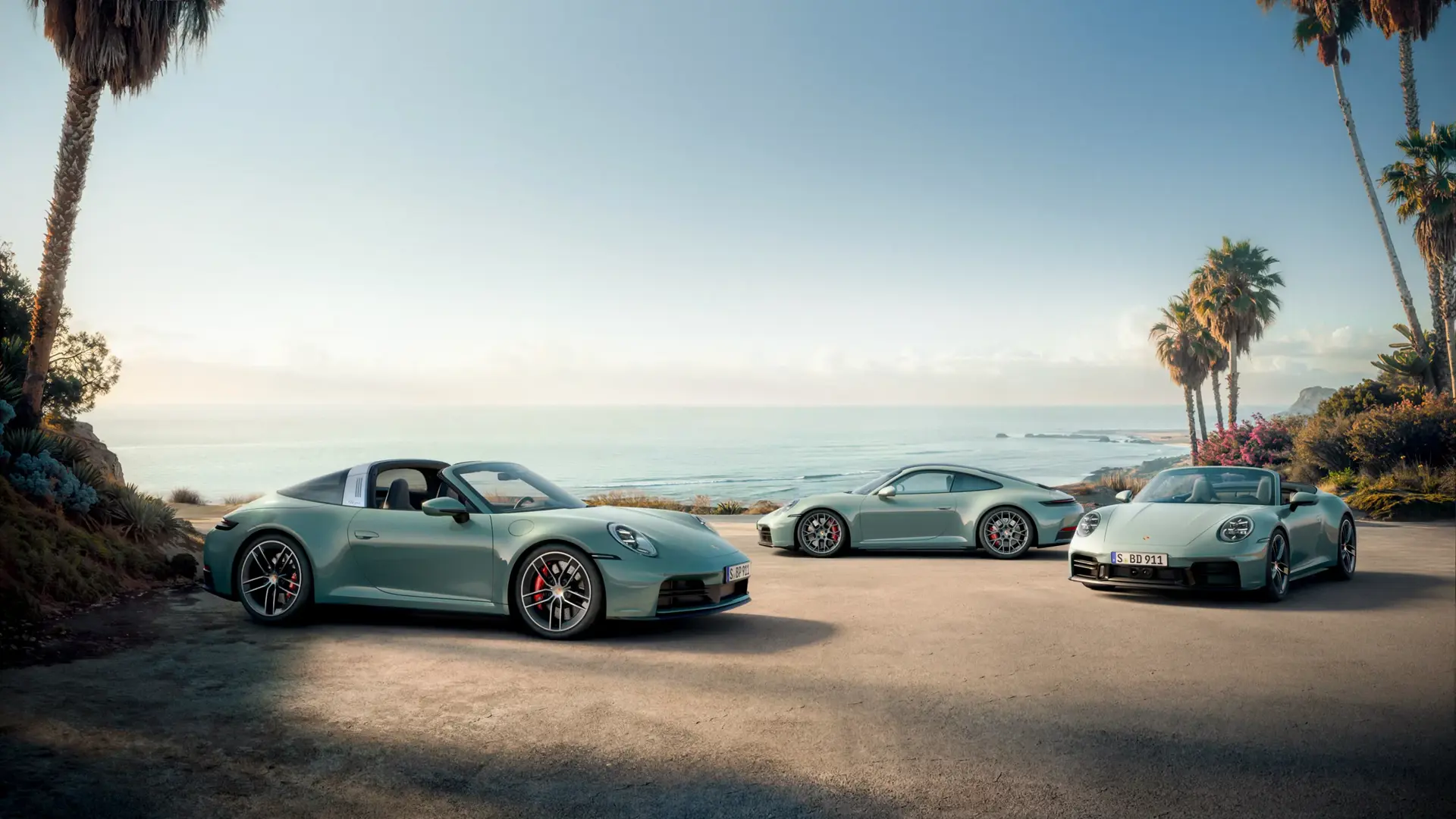 Tre lysegrønne Porsche 911 sportsvogne holder parkeret ved en kystvej med palmer og havudsigt i baggrunden.