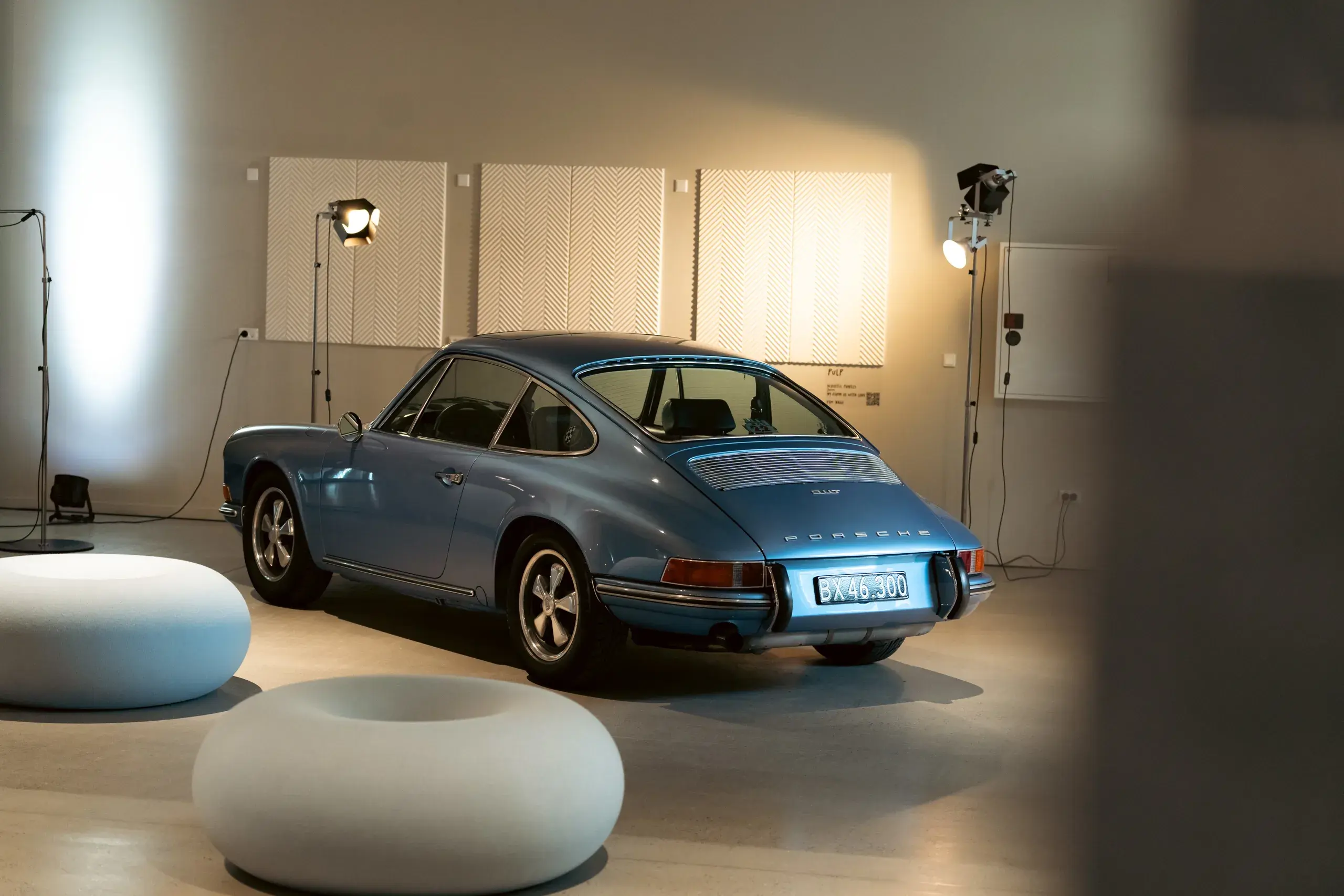Blå klassisk Porsche sportsvogn udstillet indendørs med bløde runde sæder og fotolamper omkring.