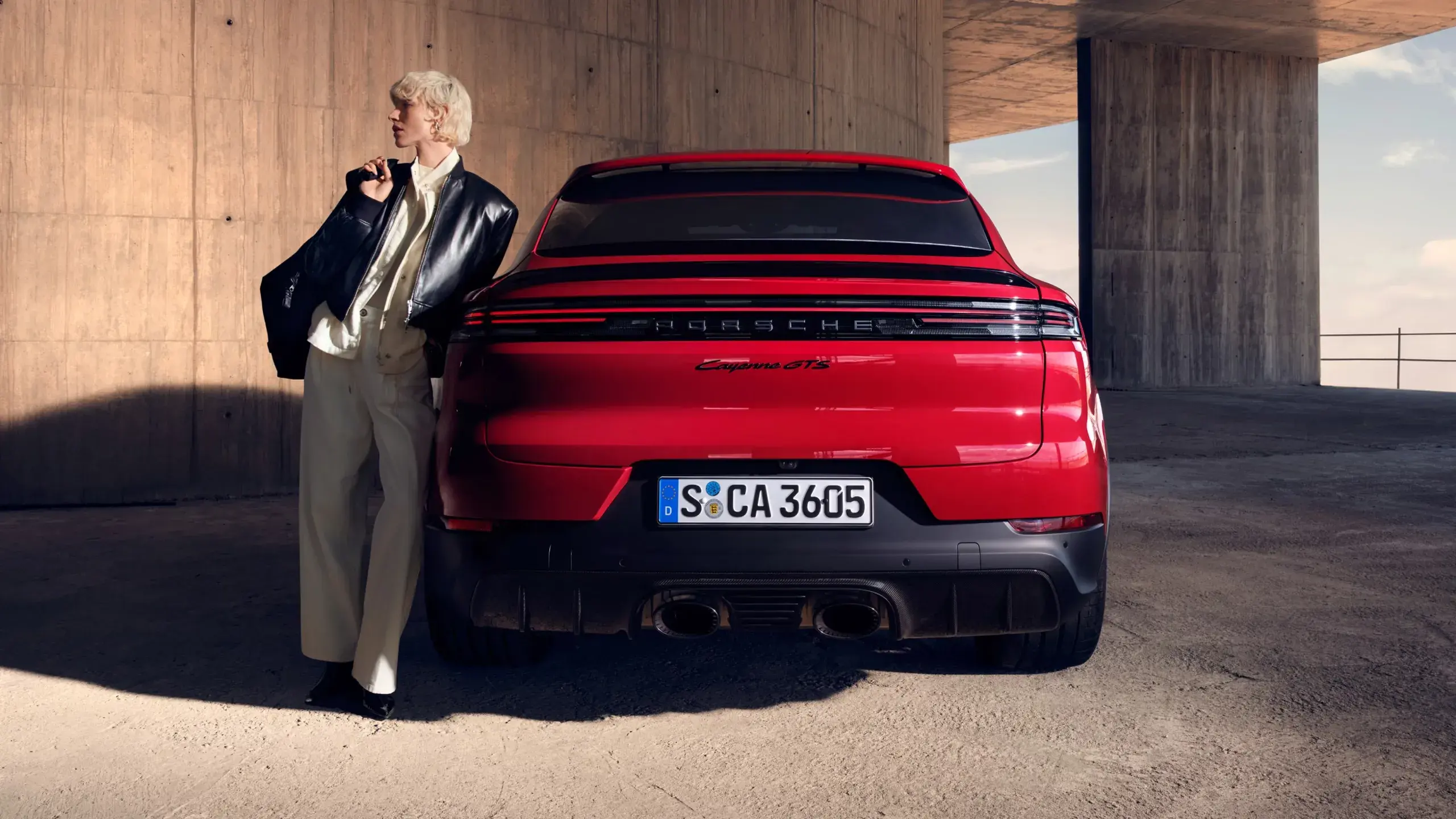 Rød Porsche Cayenne GTS Coupé holder parkeret i et råt betonmiljø med skygger på jorden.