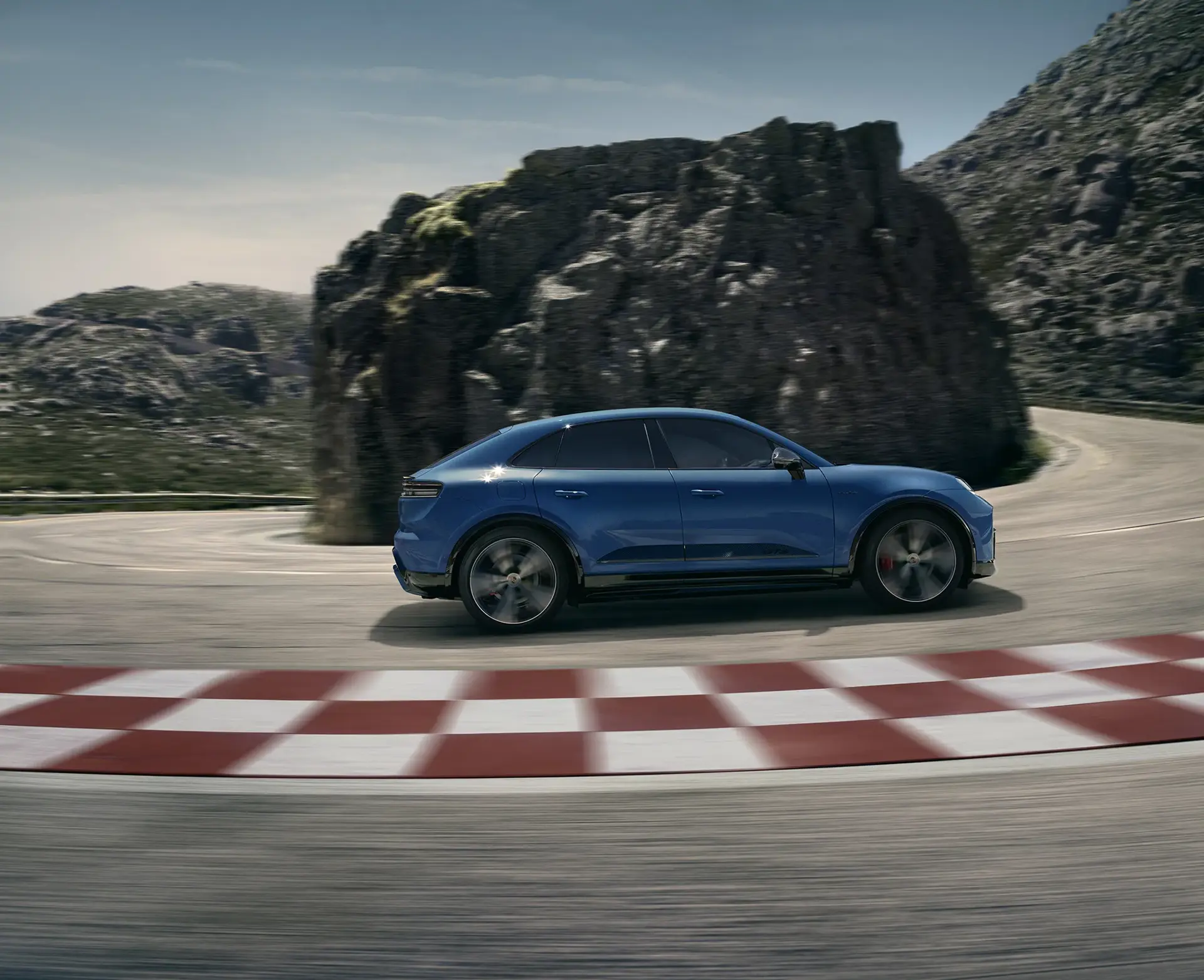 Blå sports-SUV i fart gennem et sving på en bjergvej med racerbanelignende kantmarkering.