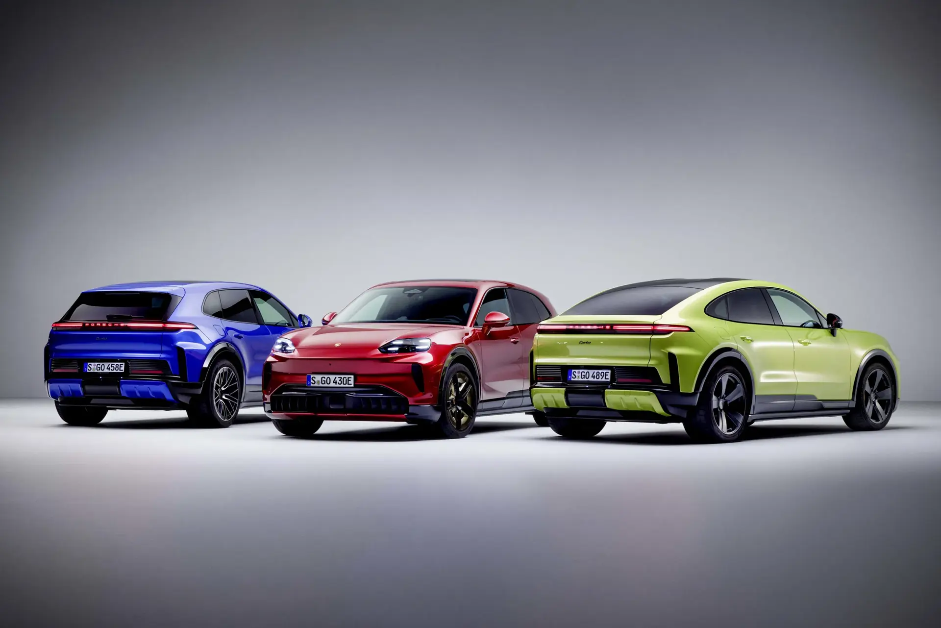 Tre Porsche Cayenne SUV’er i blå, rød og limegrøn står opstillet i et studie mod en neutral baggrund.