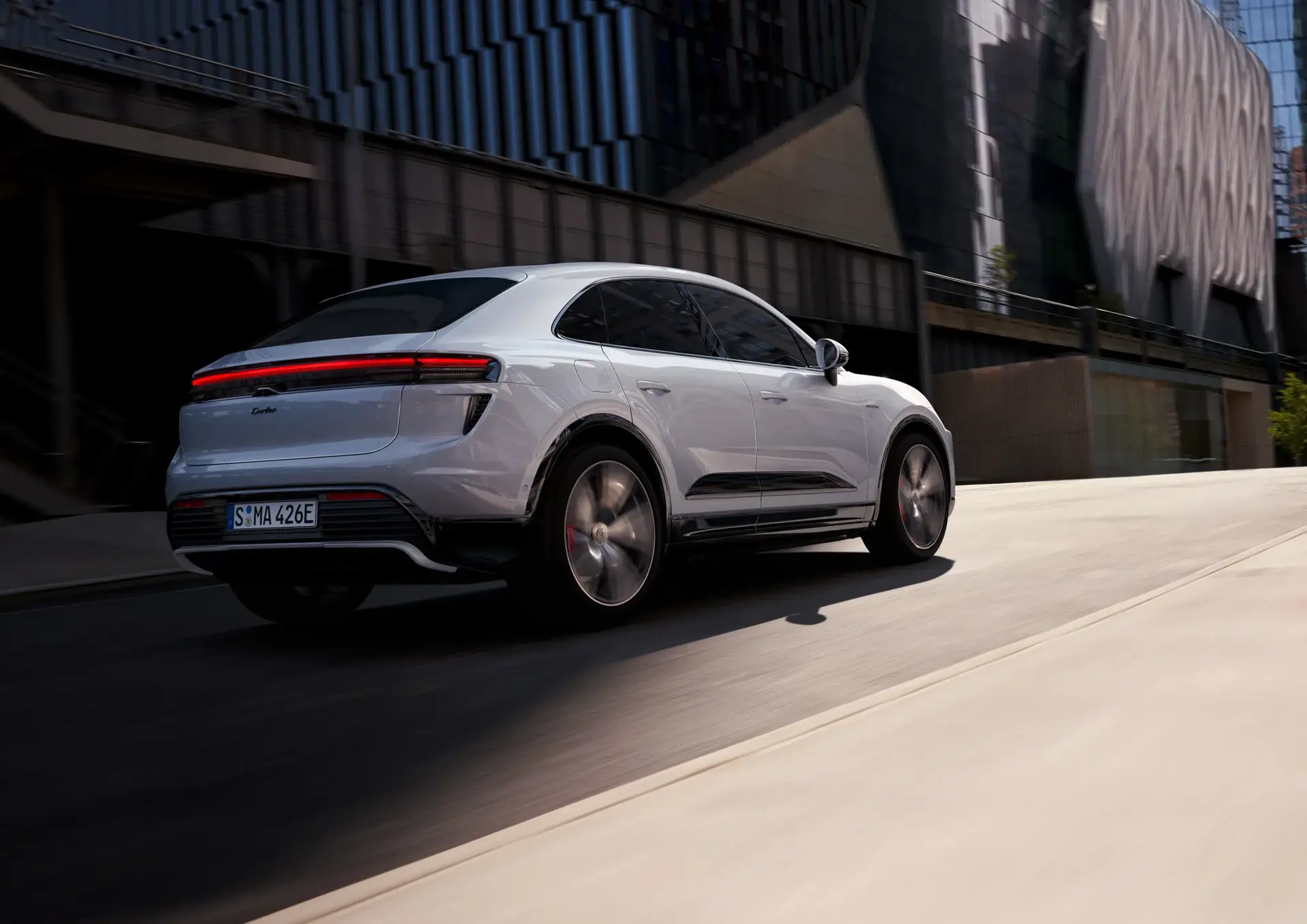 Hvid Porsche Macan Turbo ses bagfra i fart gennem en moderne by.