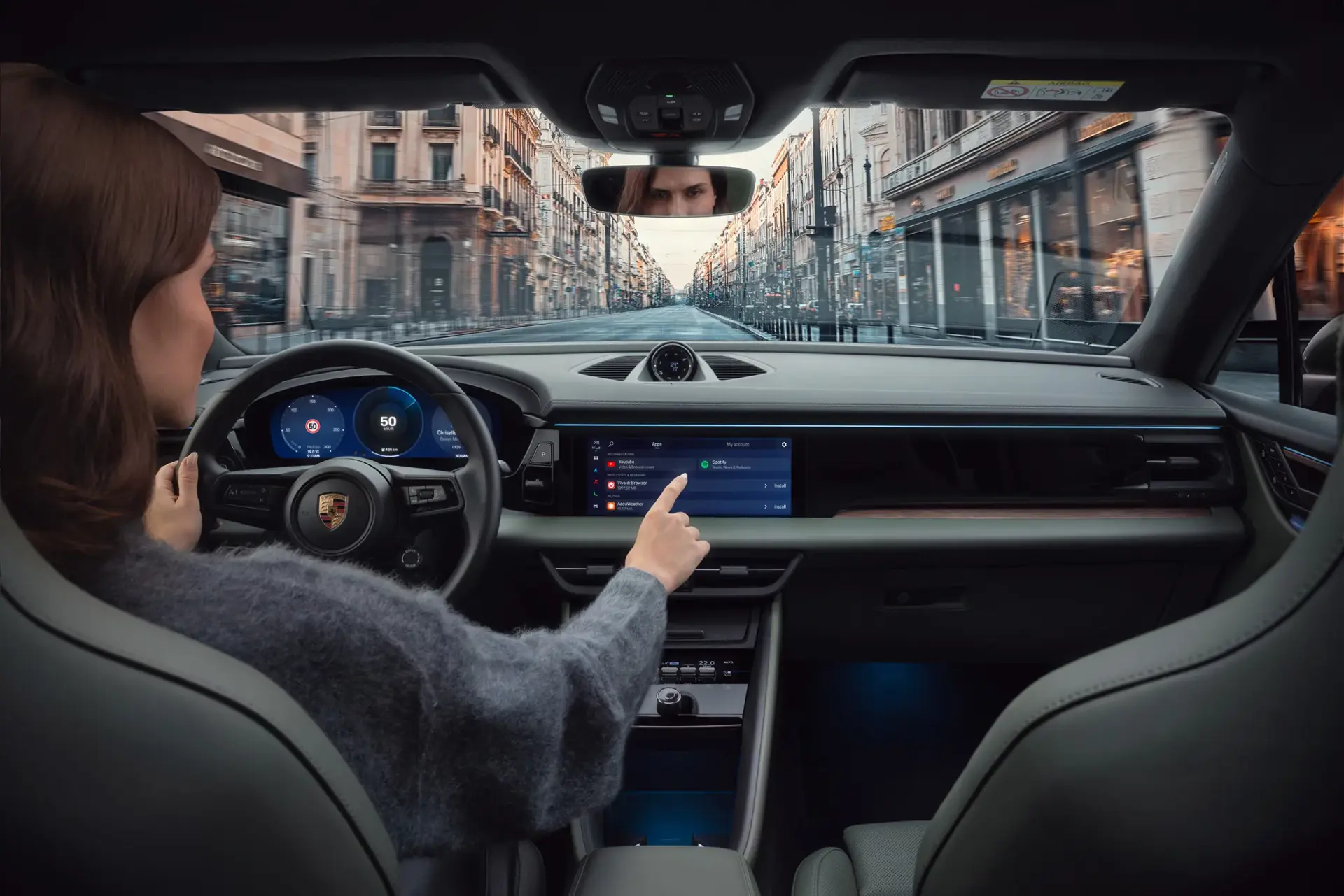 En person kører en Porsche gennem en by og bruger bilens store centrale touchskærm med Porsche Connect-funktioner.
