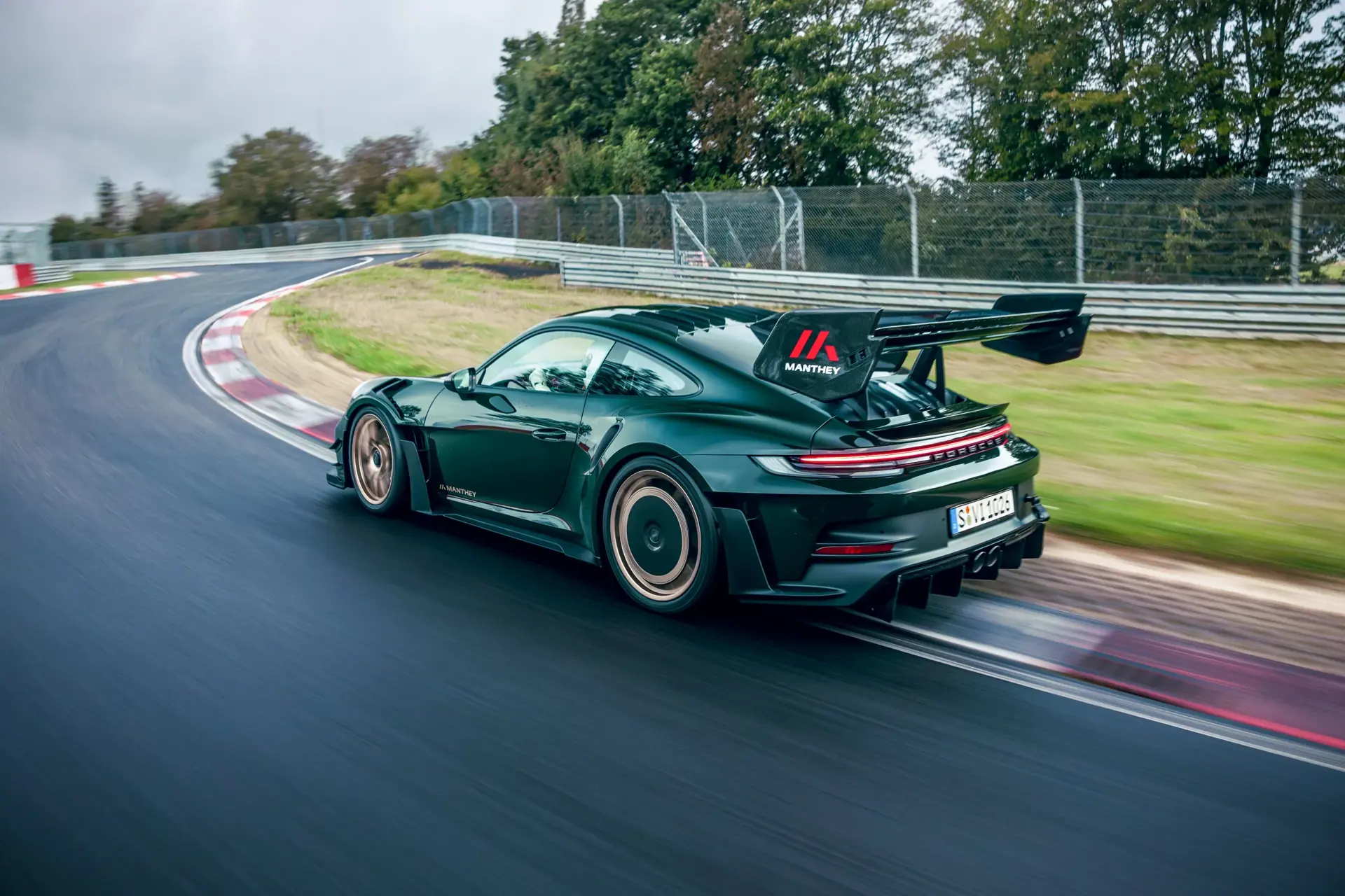 En mørkegrøn Porsche 911 GT3 med Manthey-udstyr kører hurtigt gennem en kurve på en racerbane.