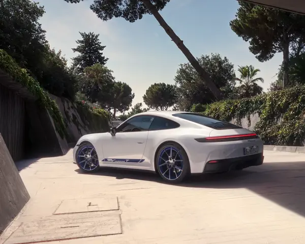 En hvid Porsche 911 Carrera T holder parkeret i sollys på en moderne, træomkranset betonvej.