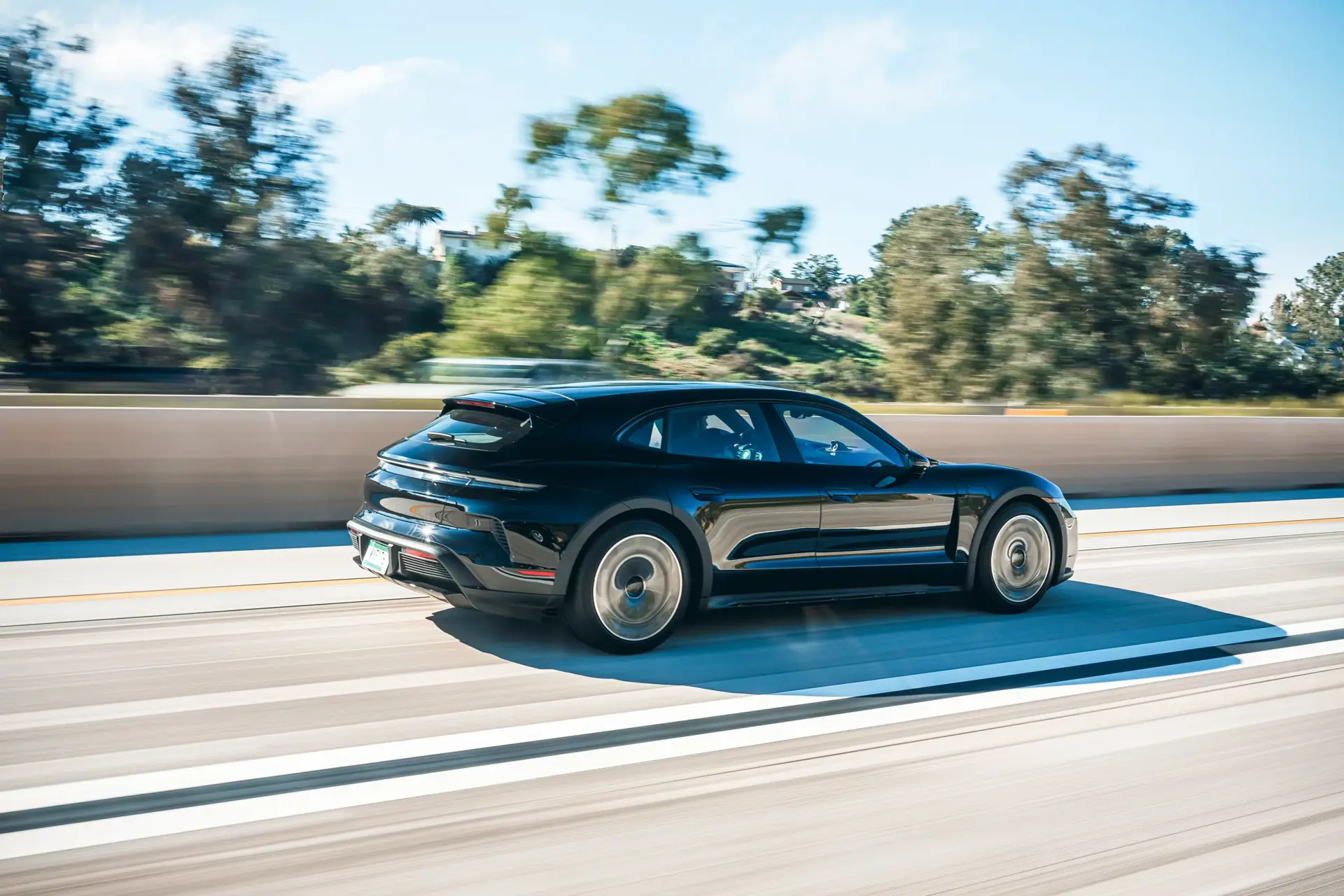Sort Porsche Taycan kører hurtigt på en motorvej i solskinsvejr.