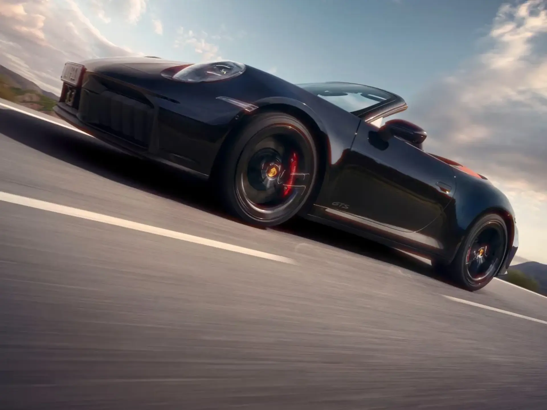 Sort Porsche 911 Carrera GTS cabriolet i fart på en åben landevej under en blå himmel.