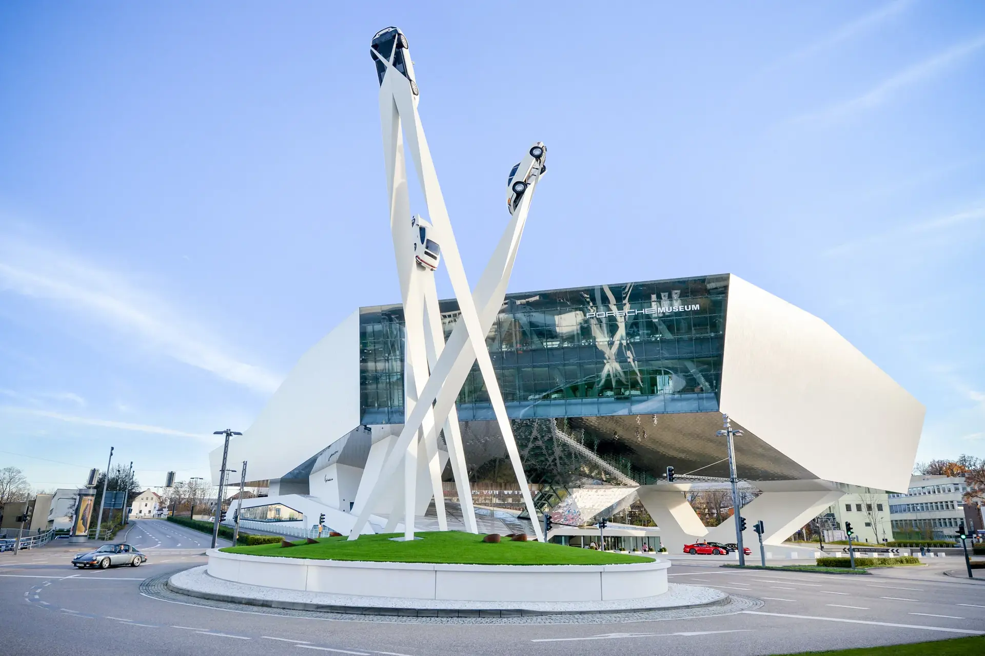 Det moderne Porsche-museum i Stuttgart med skulptur af tre biler på høje hvide søjler foran bygningen.