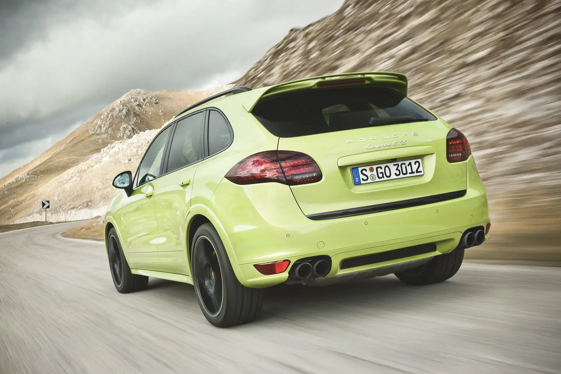 En grøn Porsche Cayenne GTS kører hurtigt på en snoet bjergvej.