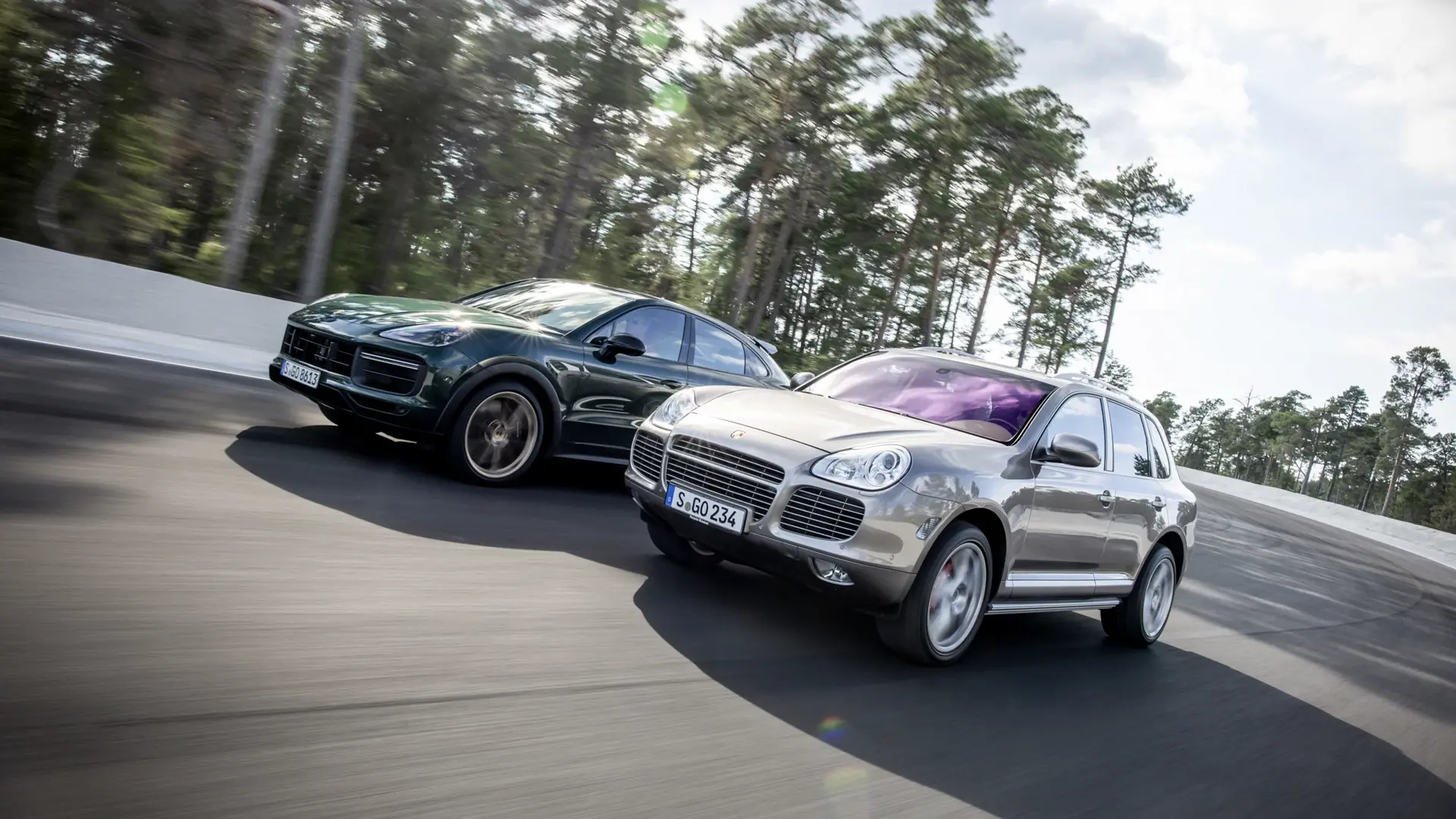 To Porsche Cayenne SUV’er kører side om side i høj fart på en racerbane omgivet af skov.