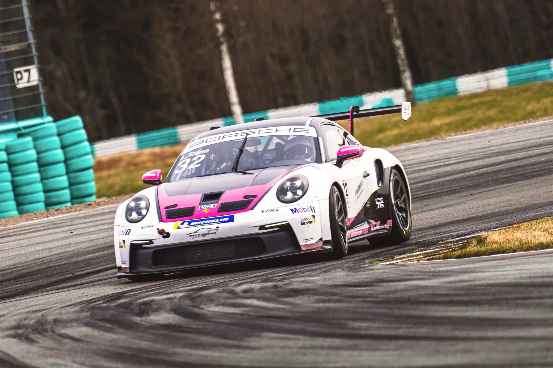 En hvid og pink Porsche-racerbil med nummer 32 tager et sving på en racerbane.