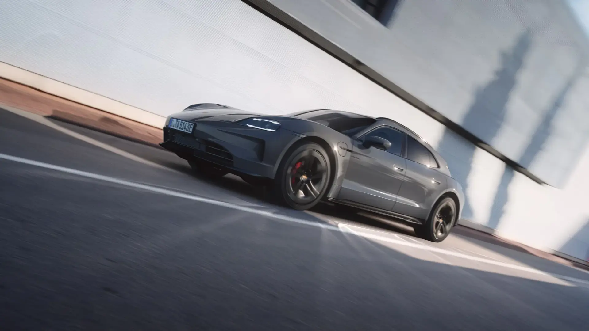 En grå Porsche Taycan GTS Sport Turismo ses i fart langs en moderne bygning.