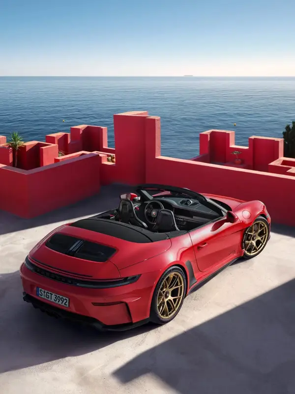 Rød Porsche 911 cabriolet parkeret ved moderne røde betonmure med udsigt over havet.