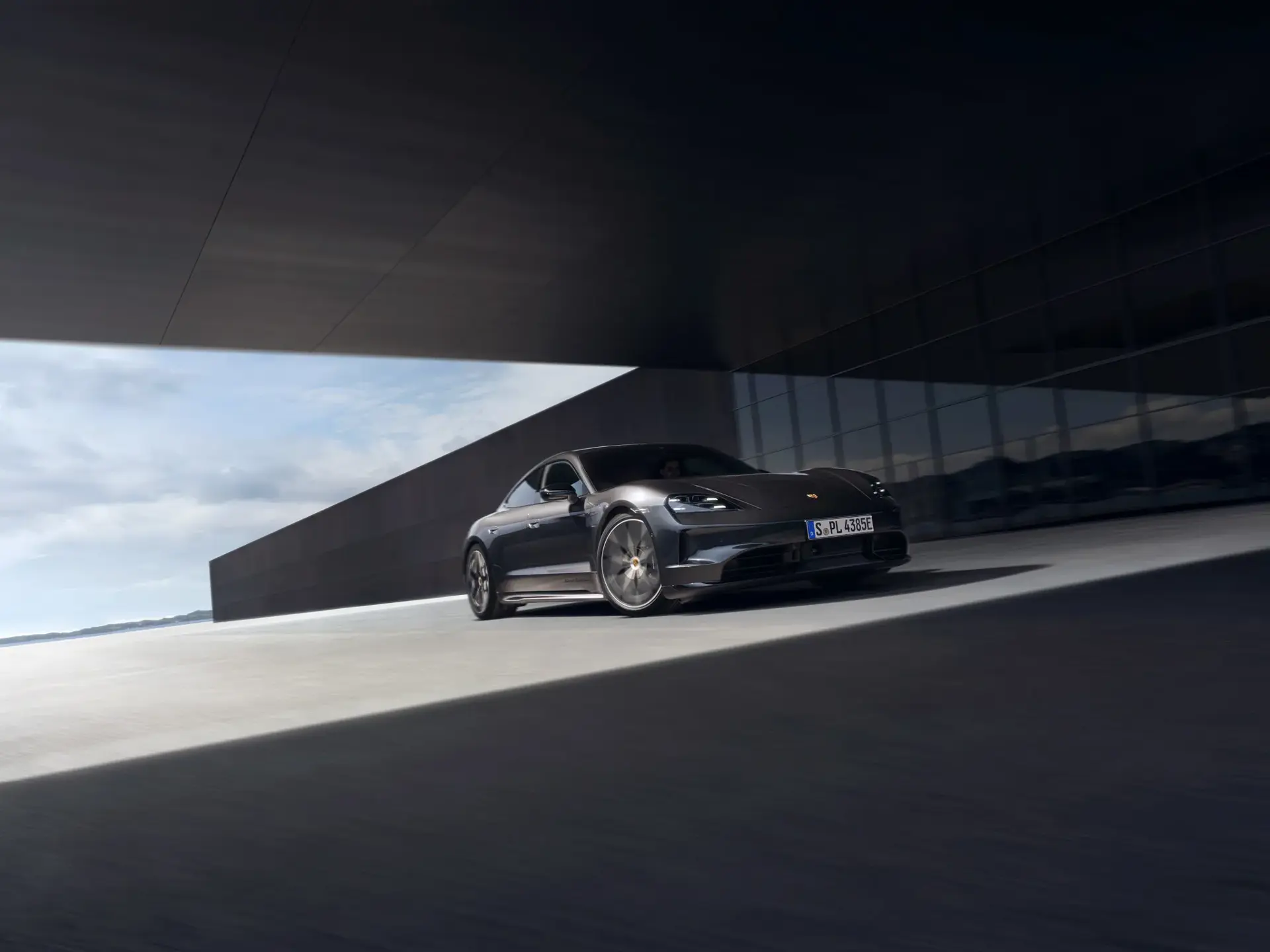Sort Porsche Taycan Black Edition kører langs en moderne, mørk bygning under en stor overdækning.