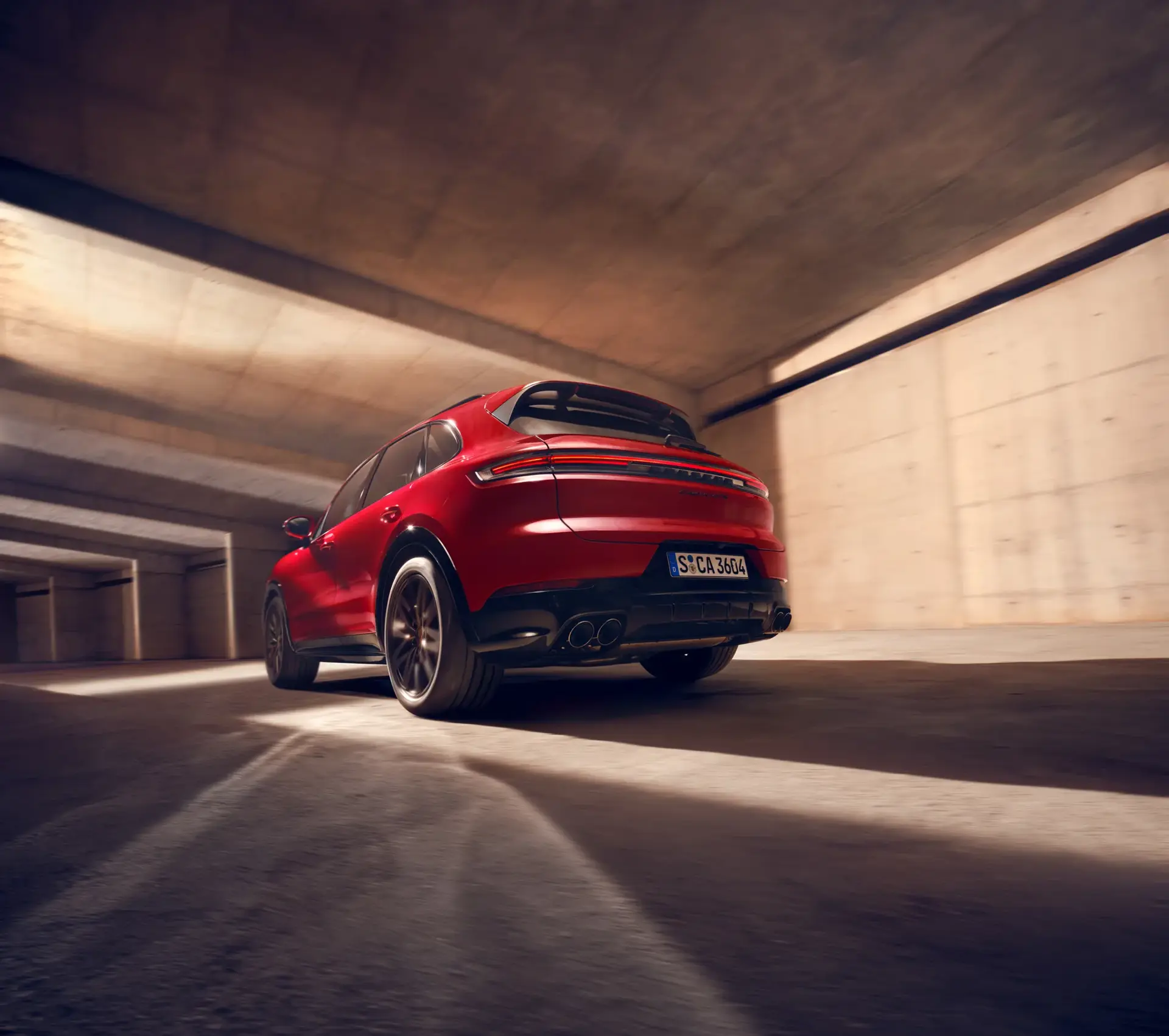 Rød Porsche Cayenne GTS set bagfra i bevægelse gennem en moderne betonparkeringskælder.