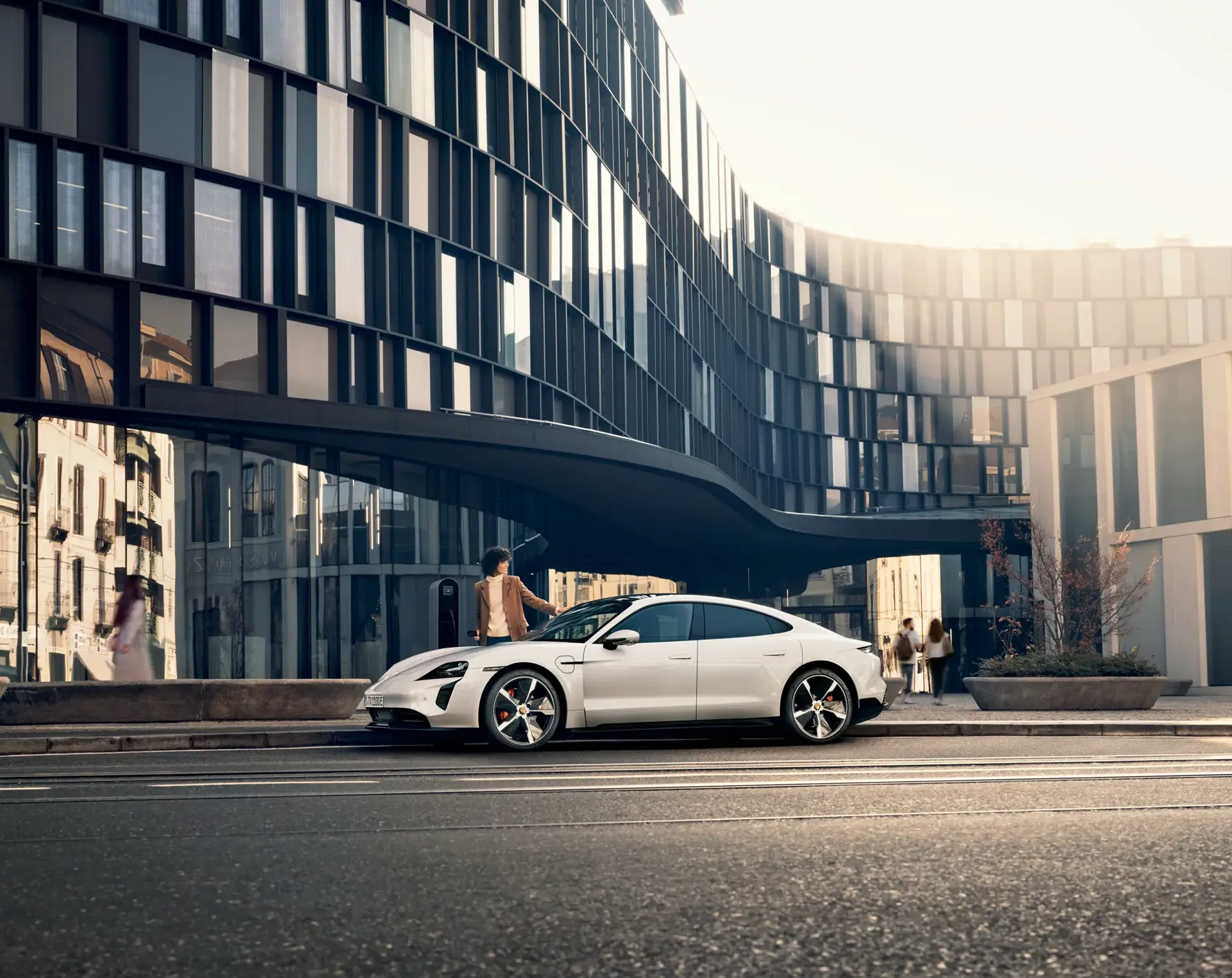 Hvid Porsche Taycan holder parkeret foran en moderne glasbygning i byen.