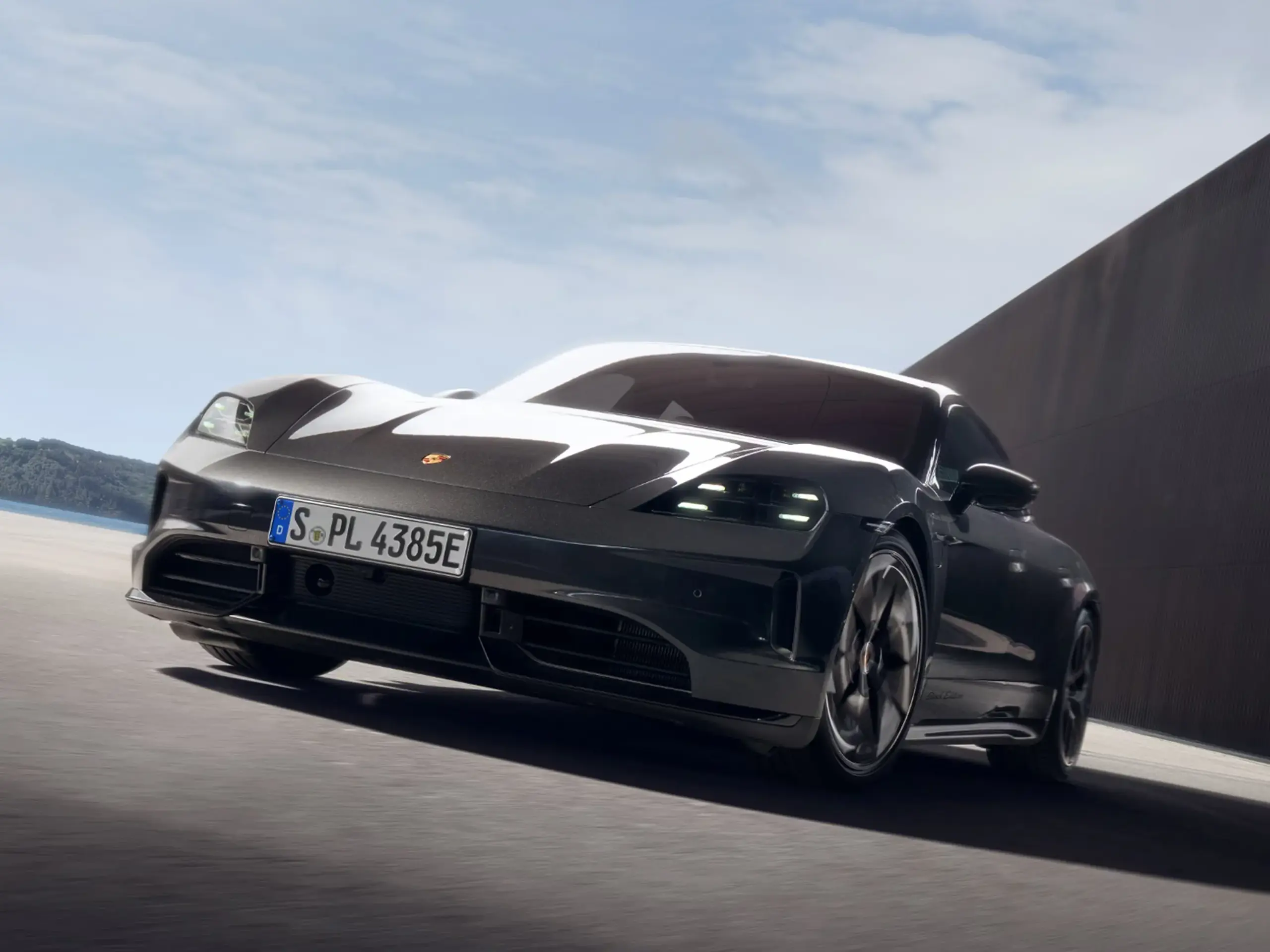 Sort Porsche Taycan Black Edition i fart på en solbeskinnet vej foran en moderne bygning.