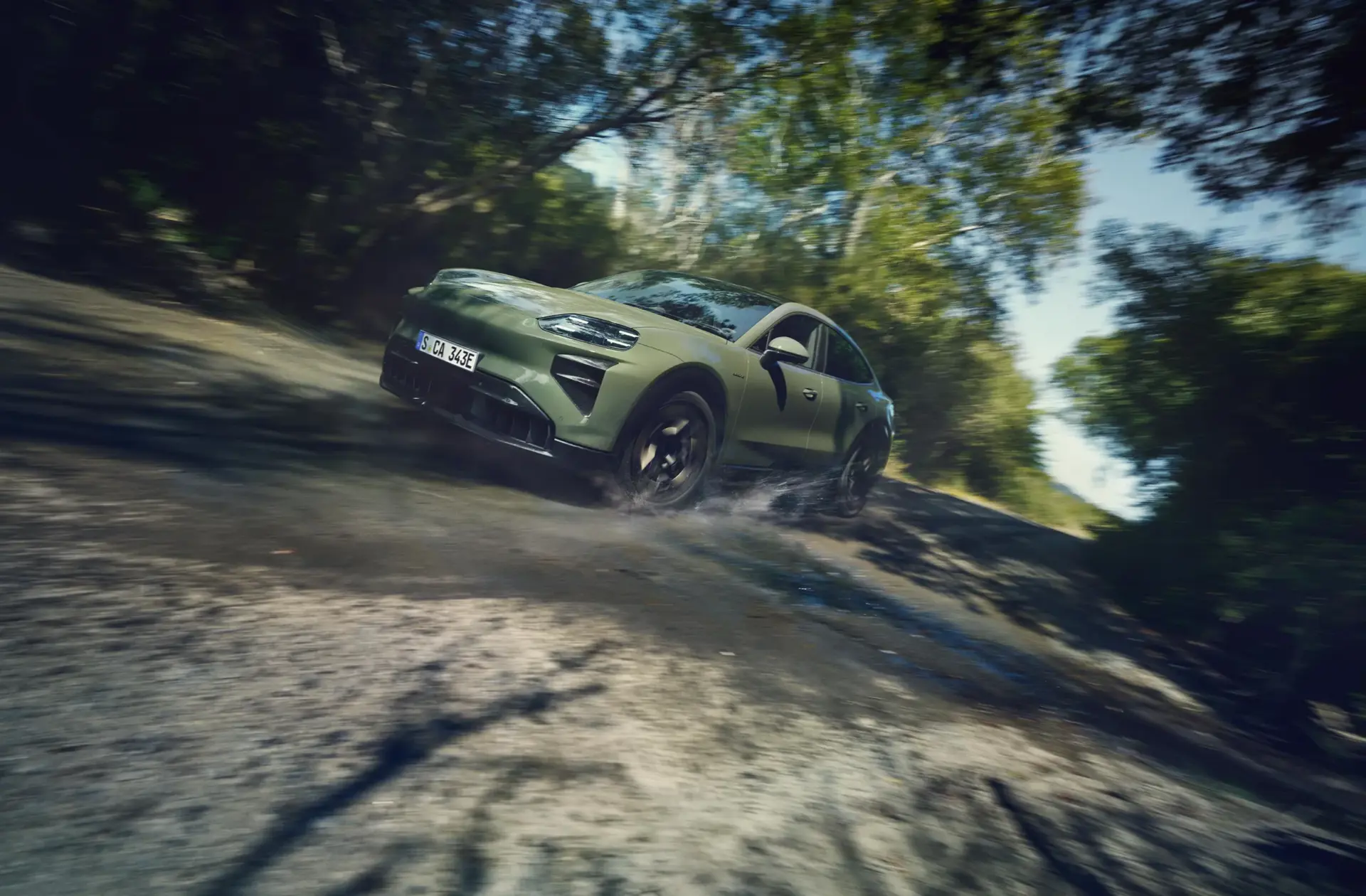Grøn elektrisk Cayenne Turbo Coupé kører hurtigt gennem en mudret skovvej med vand, der sprøjter om hjulene.