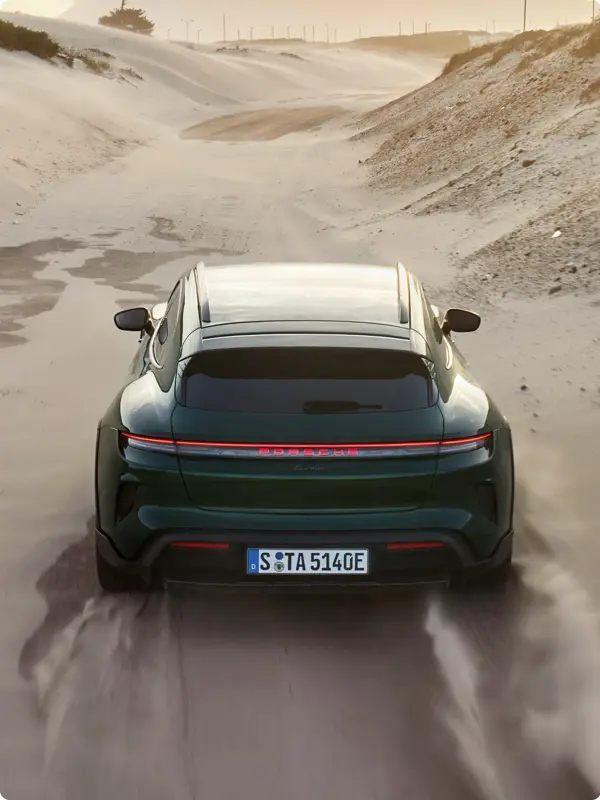 En mørkegrøn Porsche Taycan Turbo Cross Turismo ses bagfra, mens den kører hurtigt gennem et sandet ørkenlandskab.