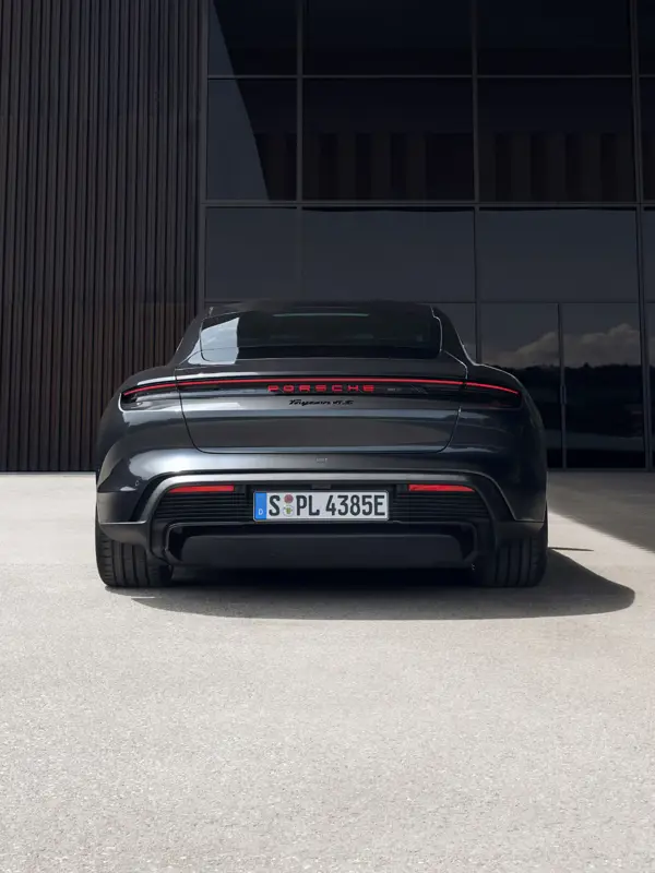 Sort Porsche Taycan set bagfra parkeret foran en moderne bygning med store glasfacader.