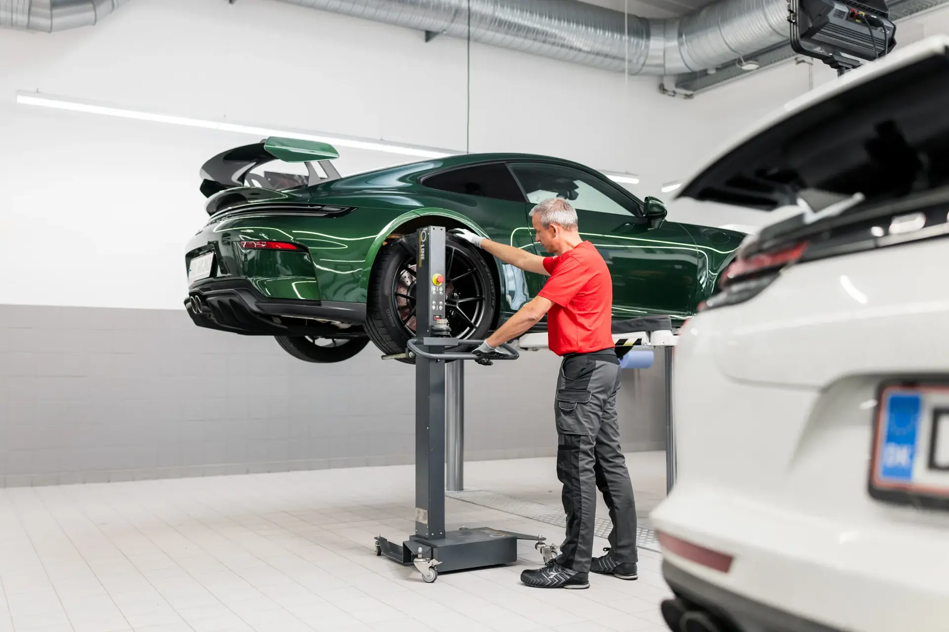 Mekaniker servicerer en grøn Porsche, der er løftet på en autolift i et lyst værksted.