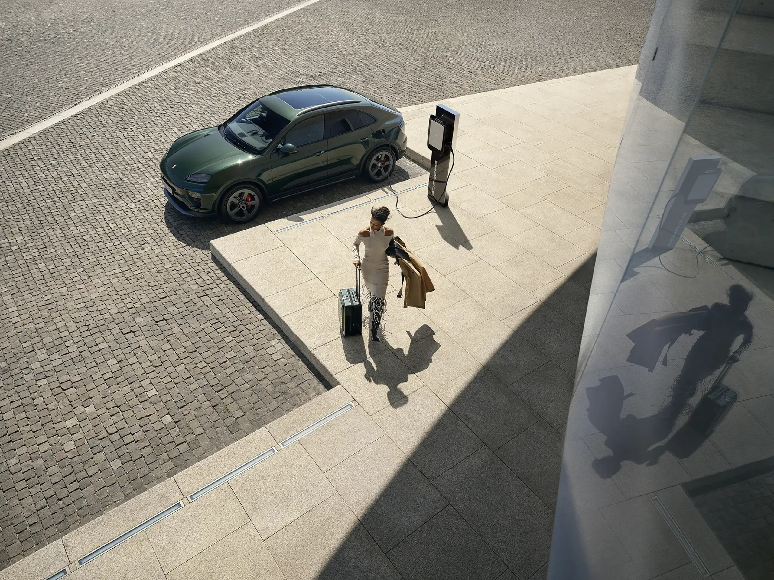 En person i grøn frakke står ved bagenden af en grøn Porsche med lysende rødt baglys og logo.