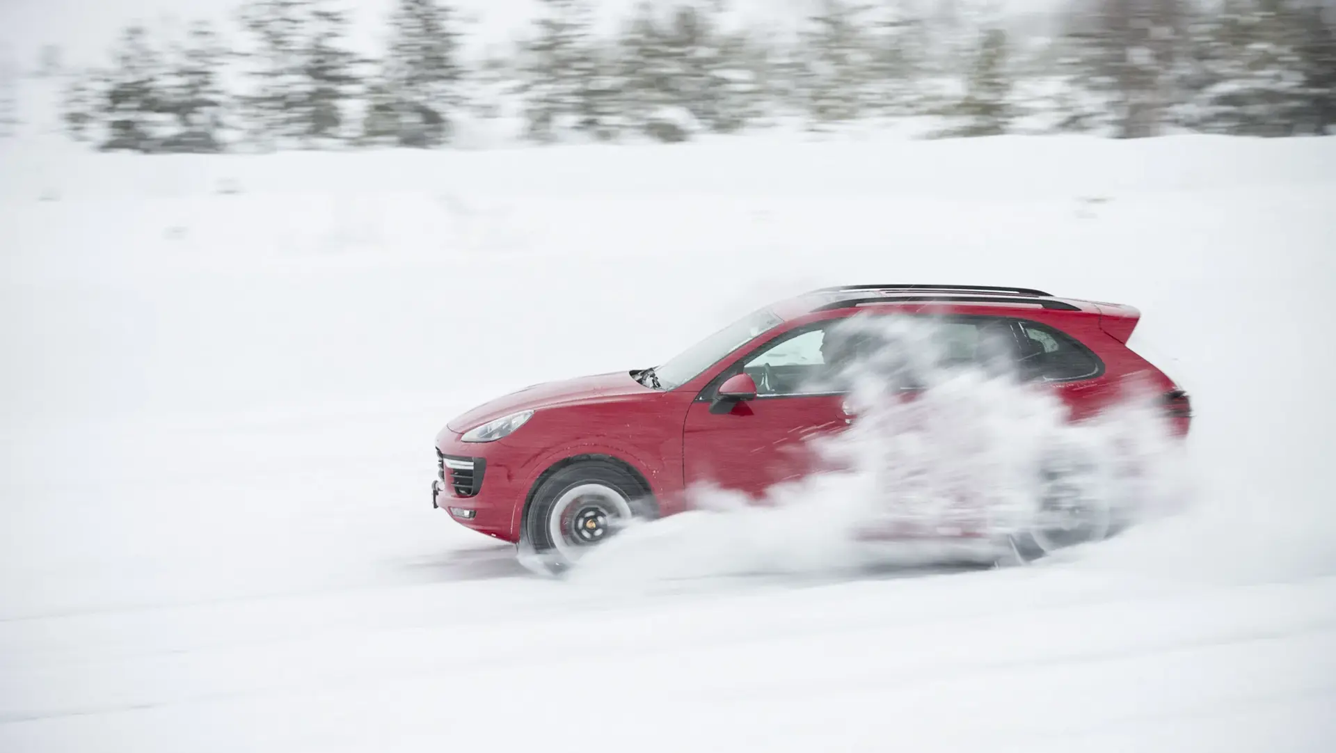 Rød SUV kører hurtigt gennem sne på en vintervej og hvirvler sne op omkring hjulene.