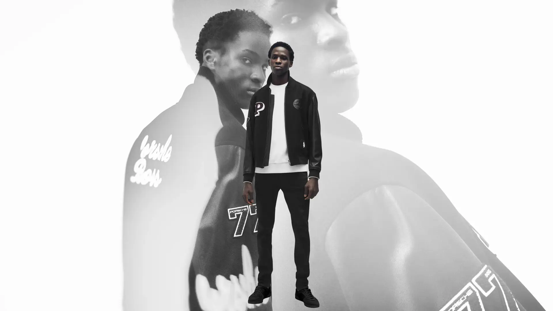 Model i sort Porsche x BOSS-jakke og joggers står foran en stor, sort-hvid baggrundsgengivelse af samme outfit.